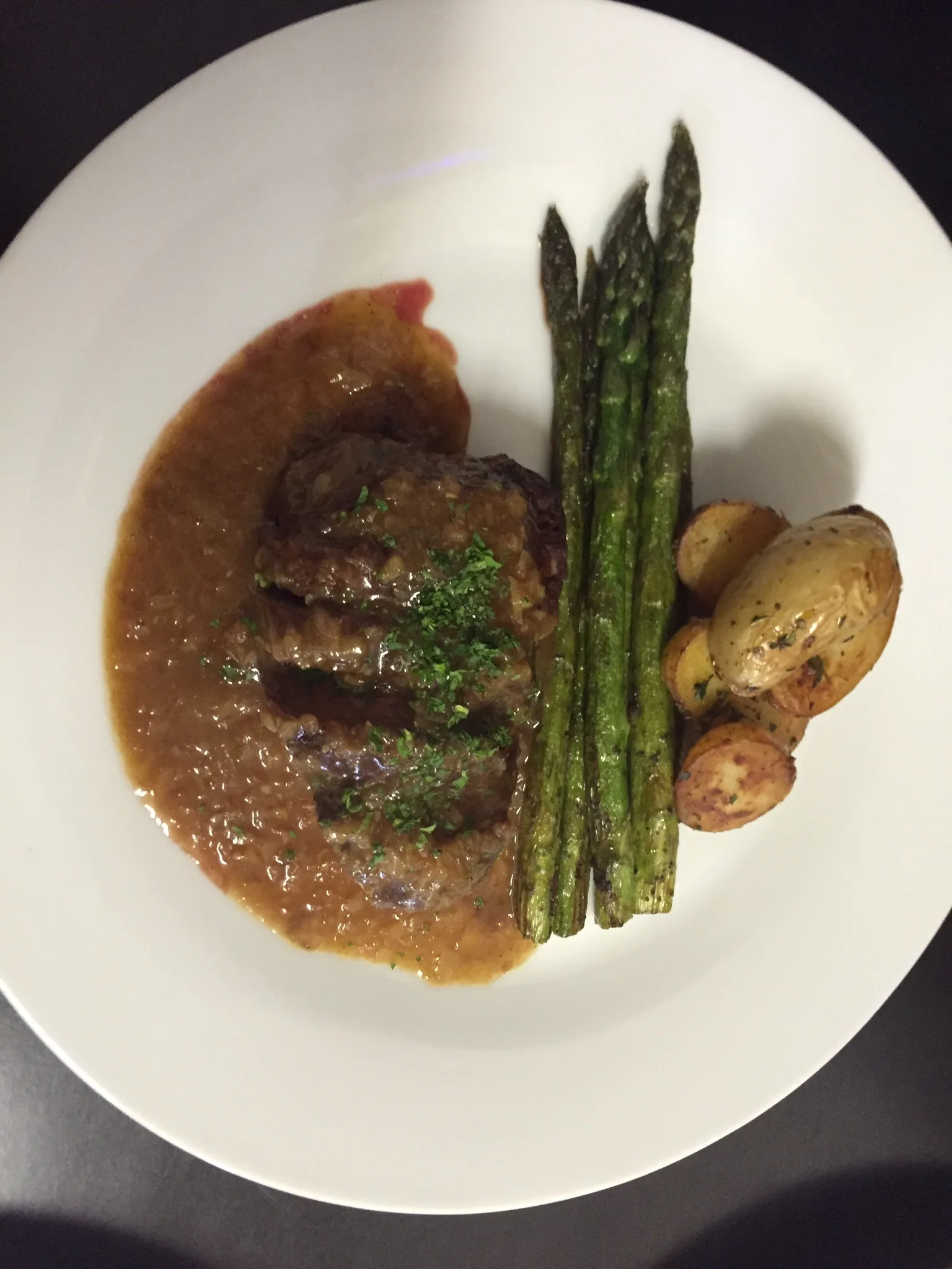 Fleischgericht in dunkler Sauce mit grünem Spargel und kleinen Kartoffeln