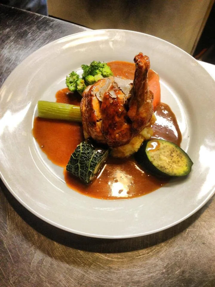 Gefülltes Geflügel mit Gemüse und Sauce auf einem weißen Teller